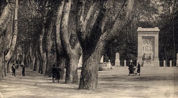 photo:à gauche allées de platanes ; a droite:le monument rectabgulaire entouré de ses 4 stèle avec mosaîque